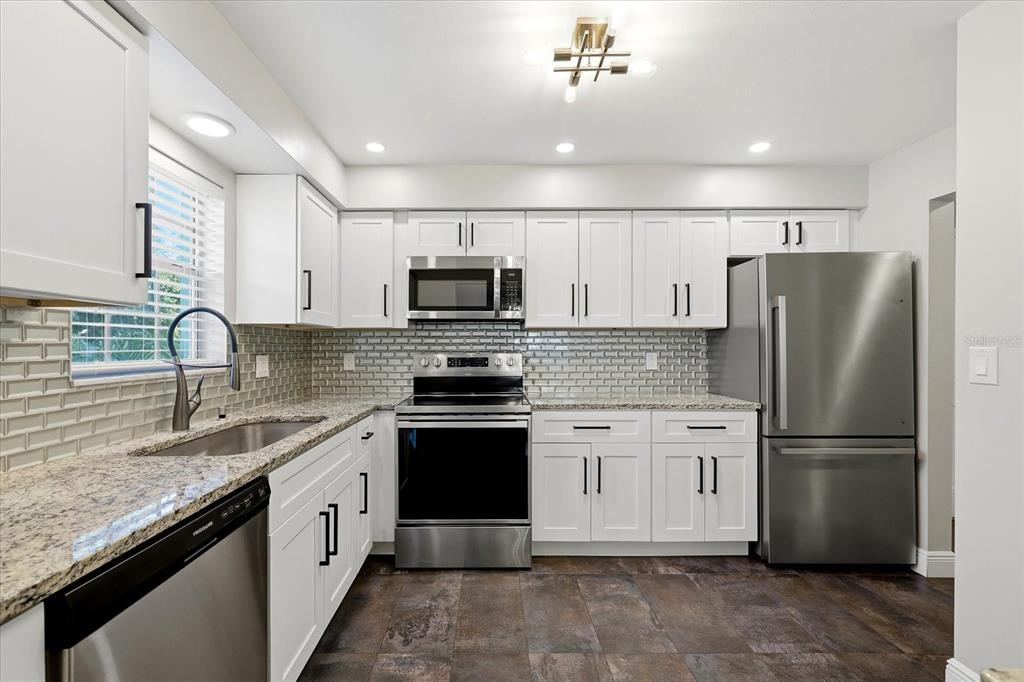 A kitchen with white cabinets, stainless steel appliances, granite countertops, and a gray subway tile backsplash — 1706 BELLEAIR FOREST DRIVE UNIT 128, BELLEAIR, FL