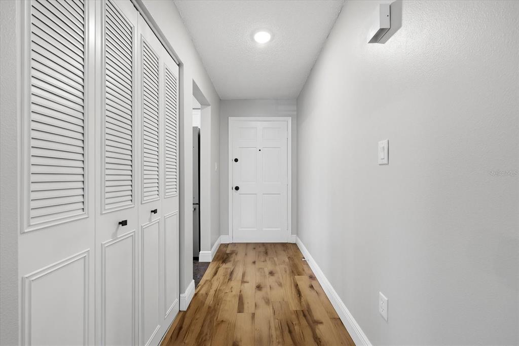 A hallway features wood-look flooring, white walls, louvered closet doors, and a white entry door — 1706 BELLEAIR FOREST DRIVE UNIT 128, BELLEAIR, FL