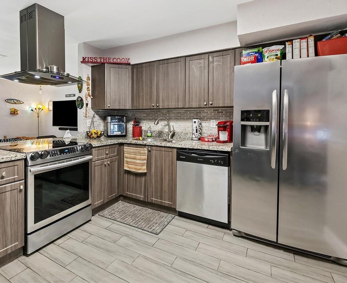 A kitchen with stainless steel appliances, wood-grain cabinets, granite countertops, and light-colored tile flooring — 4741 SW 25th Ter, Dania Beach FL 33312, DANIA BEACH, FL