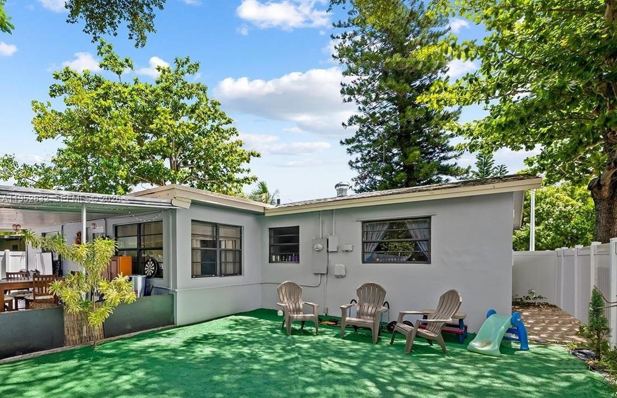 A backyard features artificial turf, three patio chairs, a small slide, and a covered patio — 4741 SW 25th Ter, Dania Beach FL 33312, DANIA BEACH, FL