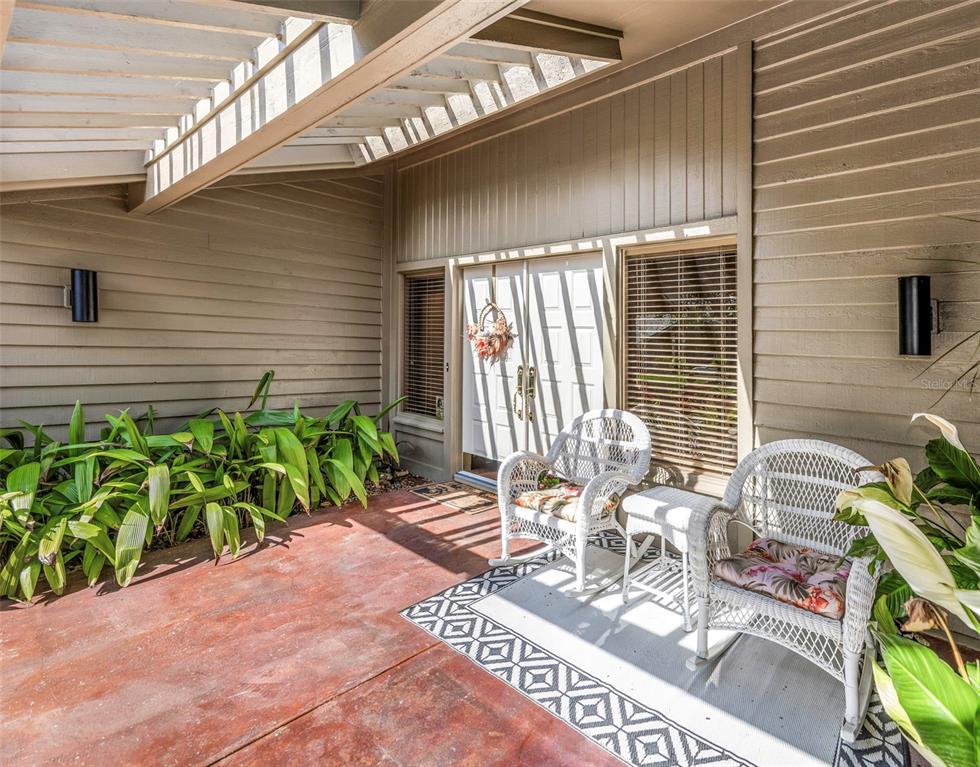 A covered patio features two white wicker rocking chairs, a patterned rug, and potted plants — 5331 SAND CRANE COURT, WESLEY CHAPEL, FL