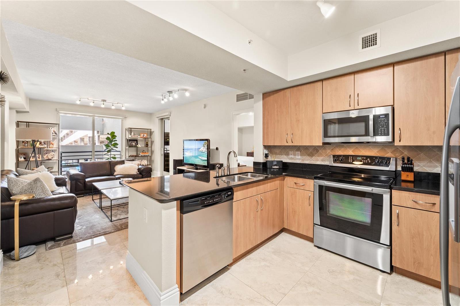 A kitchen with light wood cabinets and black countertops opens into a living room area — 1830 Radius Drive # 303, Hollywood FL 33020, HOLLYWOOD, FL