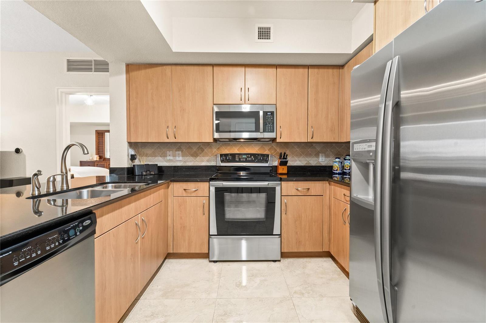A kitchen with light wood cabinets, black countertops, stainless steel appliances, and tiled flooring — 1830 Radius Drive # 303, Hollywood FL 33020, HOLLYWOOD, FL
