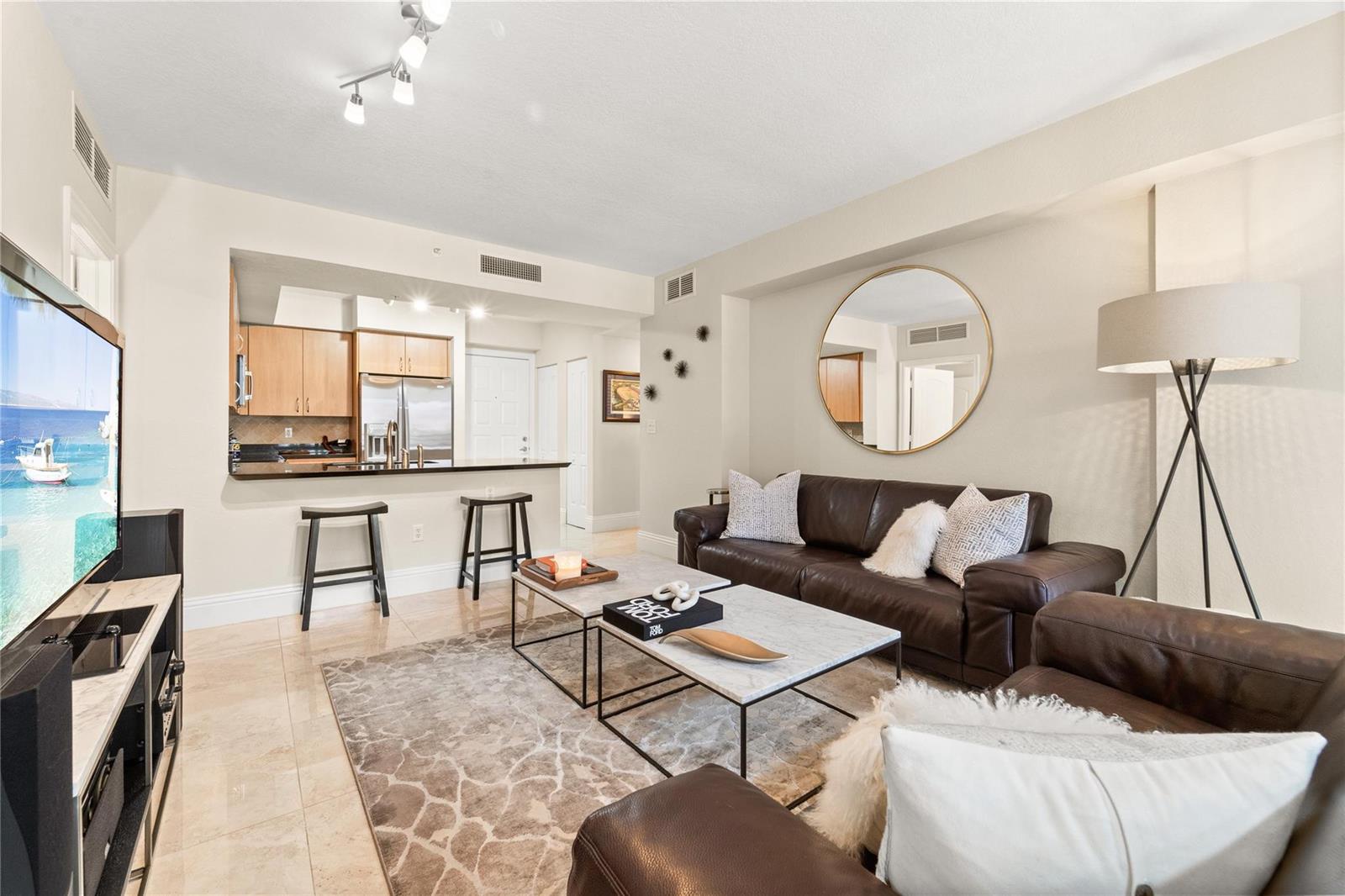 A living room features a brown leather sofa, marble coffee tables, and an open kitchen — 1830 Radius Drive # 303, Hollywood FL 33020, HOLLYWOOD, FL
