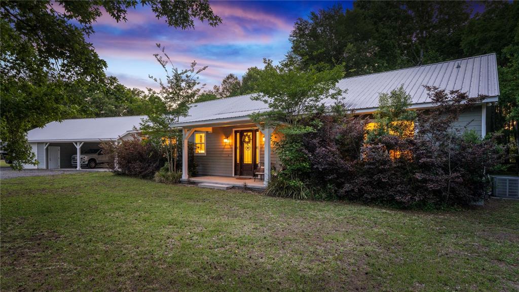A single-story house with a metal roof, front porch, and attached carport at dusk — 5901 SOLANA STREET, ELKTON, FL