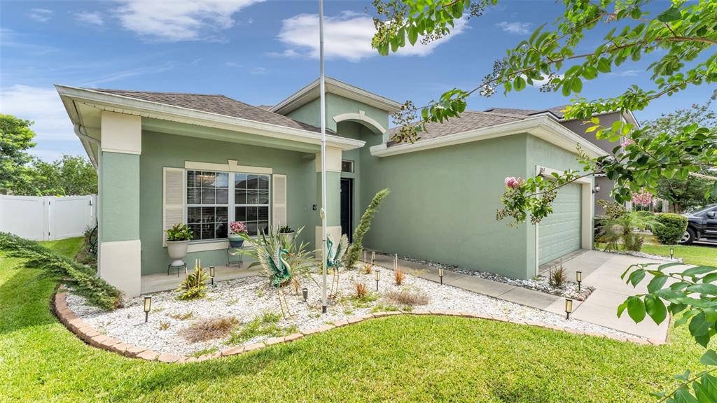 A single-story house with green stucco walls, a white-trimmed window, and a white rock garden — 1053 KRENSON WOODS ROAD, LAKELAND, FL