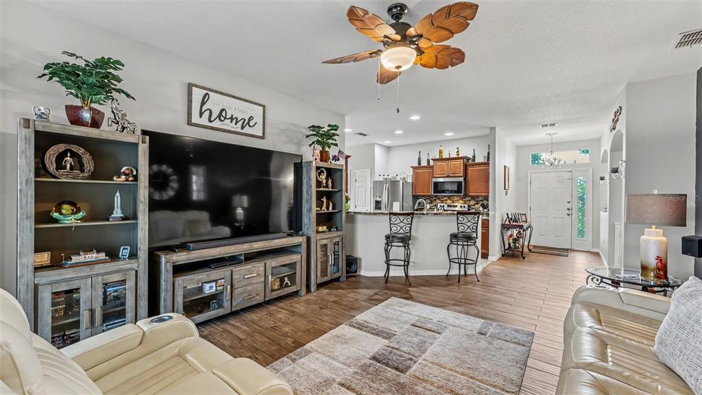 A living room with a large television, wooden media console, and an open kitchen area — 1053 KRENSON WOODS ROAD, LAKELAND, FL