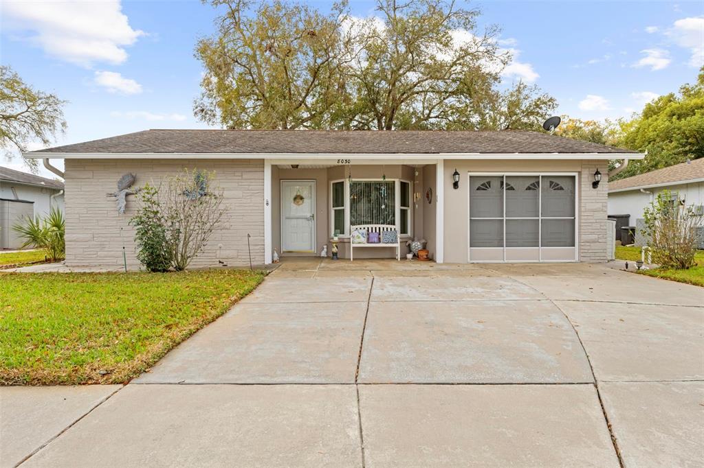 A single-story house with a concrete driveway, stone facade, and a screened-in garage door — 8030 GLENEAGLE DRIVE, PORT RICHEY, FL