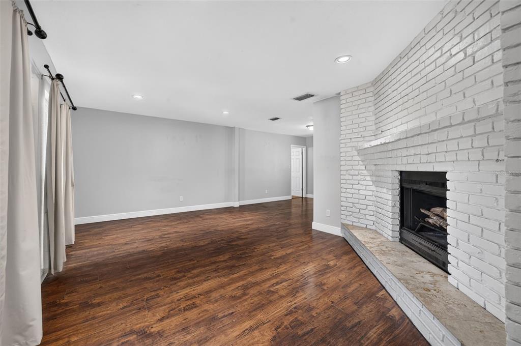 A living room with dark wood flooring, grey walls, and a white painted brick fireplace — 112 ROOSEVELT PLACE, MAITLAND, FL