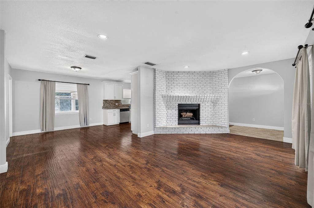 A living room with wood floors, a white brick fireplace, and an adjacent kitchen area — 112 ROOSEVELT PLACE, MAITLAND, FL