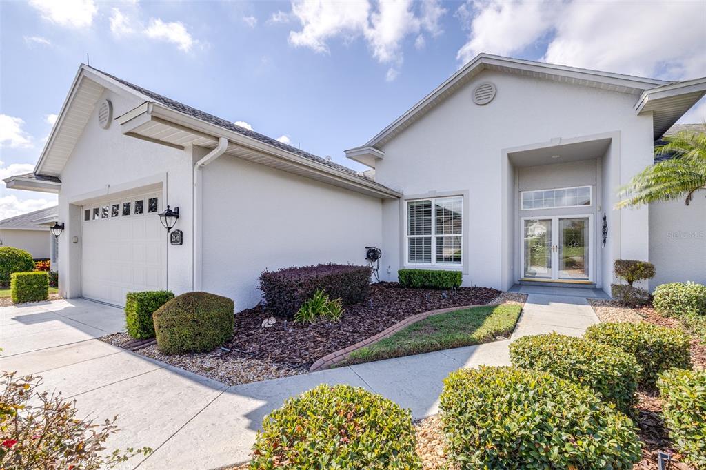 A single-story house exterior features a white stucco facade, a garage, and a front entrance — 2636 HUNTINGTON HILLS DRIVE, LAKELAND, FL