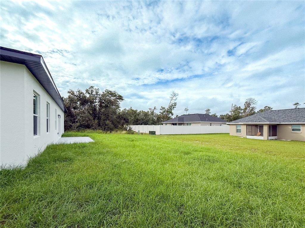 A view of a grassy backyard between two houses with a white vinyl fence — 15716 SW 46TH AVENUE ROAD, OCALA, FL