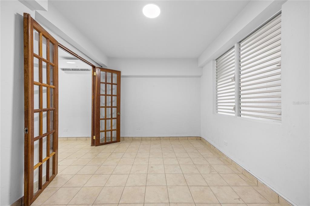 An empty room features light-colored tile flooring, white walls, and wooden French doors — CAPARRA HEIGHTS J-42 ESCORIAL AVENUE UNIT 603, SAN JUAN, PR