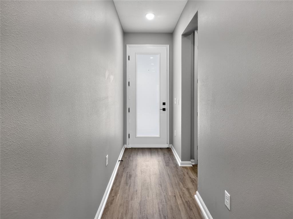 A narrow hallway features gray walls, wood-look flooring, and a white door with a glass panel — 992 GRIFFON AVENUE, LAKE ALFRED, FL