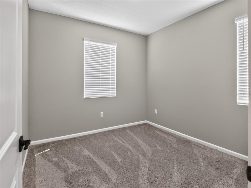 An empty bedroom with gray walls, carpeted flooring, and two windows with white blinds — 992 GRIFFON AVENUE, LAKE ALFRED, FL
