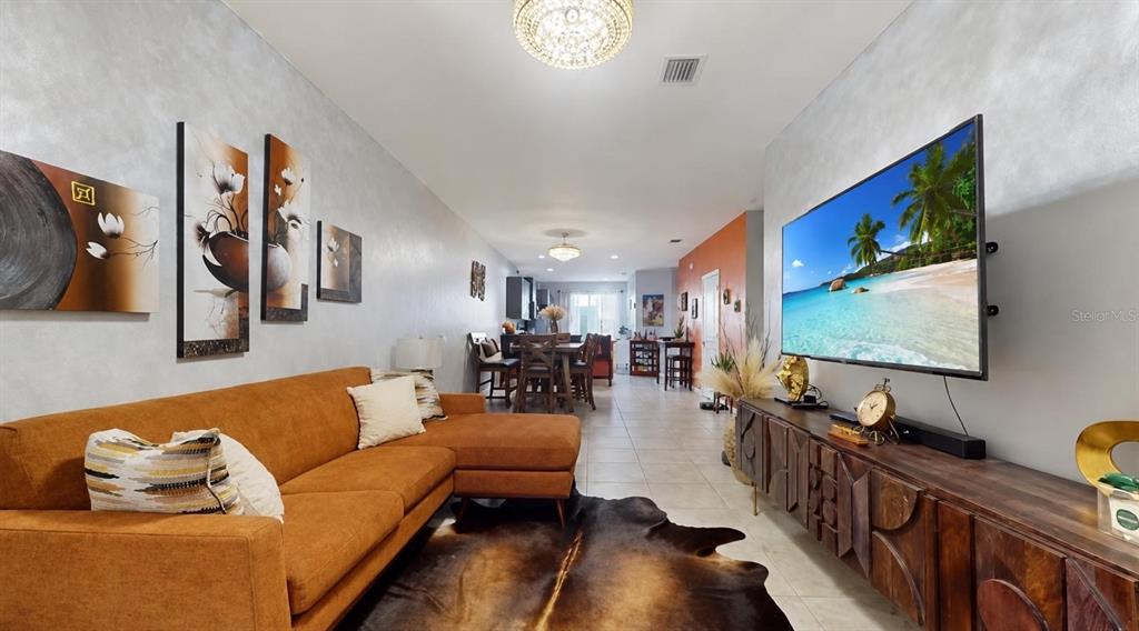 A living room features an orange sectional sofa, a cowhide rug, and a wall-mounted television — 1452 SE 24TH AVE, HOMESTEAD, FL