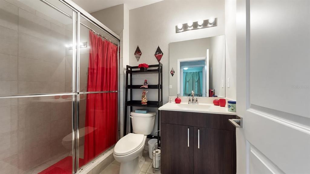 A bathroom features a glass-enclosed shower, a toilet with shelving, and a dark wood vanity — 1452 SE 24TH AVE, HOMESTEAD, FL