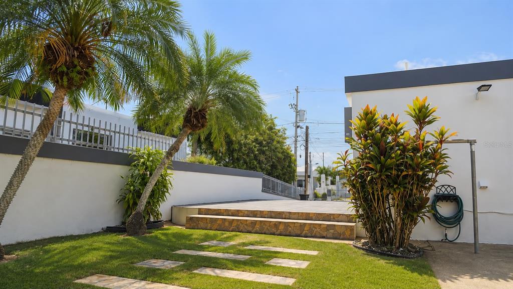 A grassy yard features stone pavers, a tiered patio, and palm trees beside a building — PR-651 KM 3.2. SR 651, ARECIBO, PR