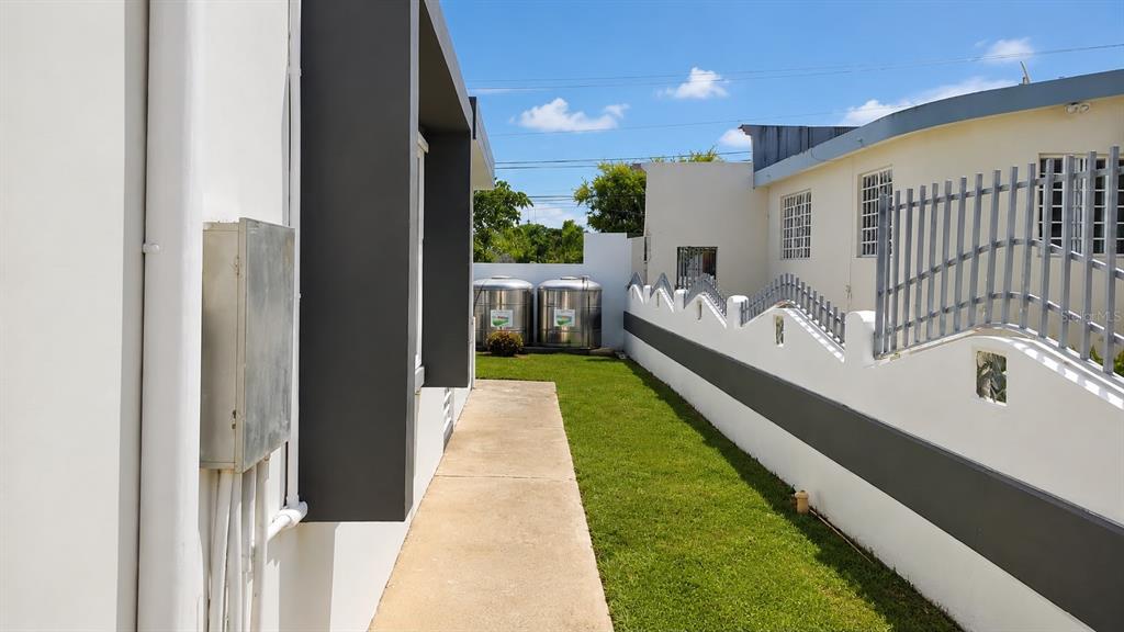 A narrow concrete walkway runs between a white building and a tall perimeter wall — PR-651 KM 3.2. SR 651, ARECIBO, PR