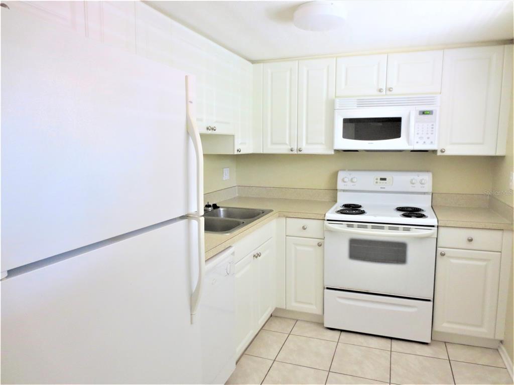 A kitchen features white cabinets, white appliances, a double sink, and light-colored tile flooring — 5310 26TH STREET W UNIT 1105, BRADENTON, FL