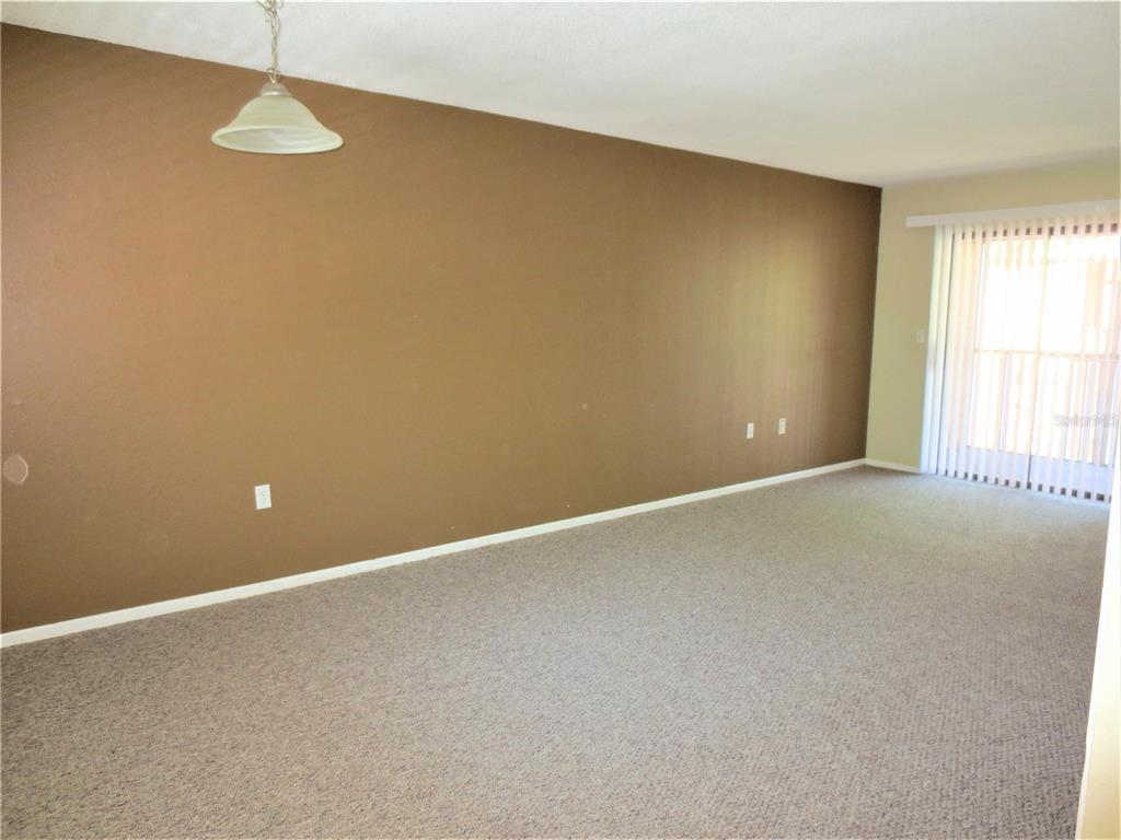 An empty living room features a large brown accent wall, beige carpet, and sliding doors — 5310 26TH STREET W UNIT 1105, BRADENTON, FL