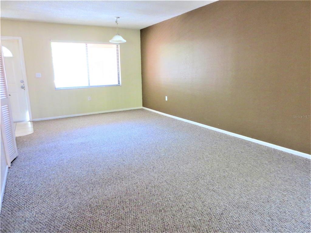 An empty living room features beige carpet, light walls, and one dark brown accent wall — 5310 26TH STREET W UNIT 1105, BRADENTON, FL