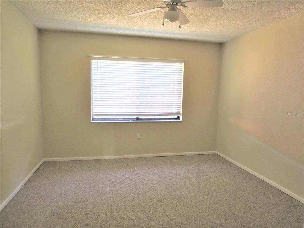 An empty bedroom features beige walls, gray carpeting, and a ceiling fan — 5310 26TH STREET W UNIT 1105, BRADENTON, FL