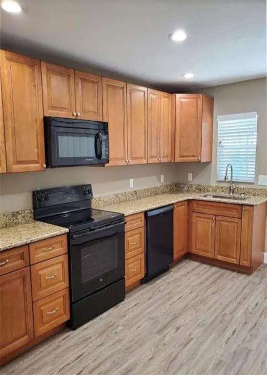 A kitchen features honey-oak cabinets, black appliances, granite countertops, and light-colored wood-look flooring — 9445 N MANASHEE DRIVE, CITRUS SPRINGS, FL