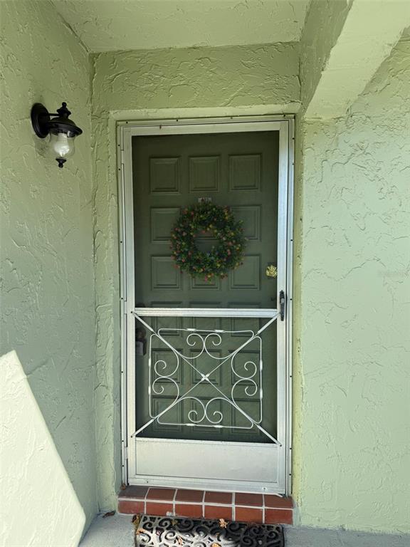A green front door with a decorative screen door and wreath sits in a stucco entryway — 1250 S PINELLAS AVENUE UNIT 802, TARPON SPRINGS, FL