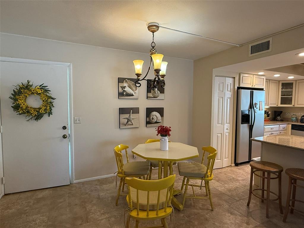 A dining area features a yellow table and chairs, a chandelier, and coastal wall art — 1250 S PINELLAS AVENUE UNIT 802, TARPON SPRINGS, FL