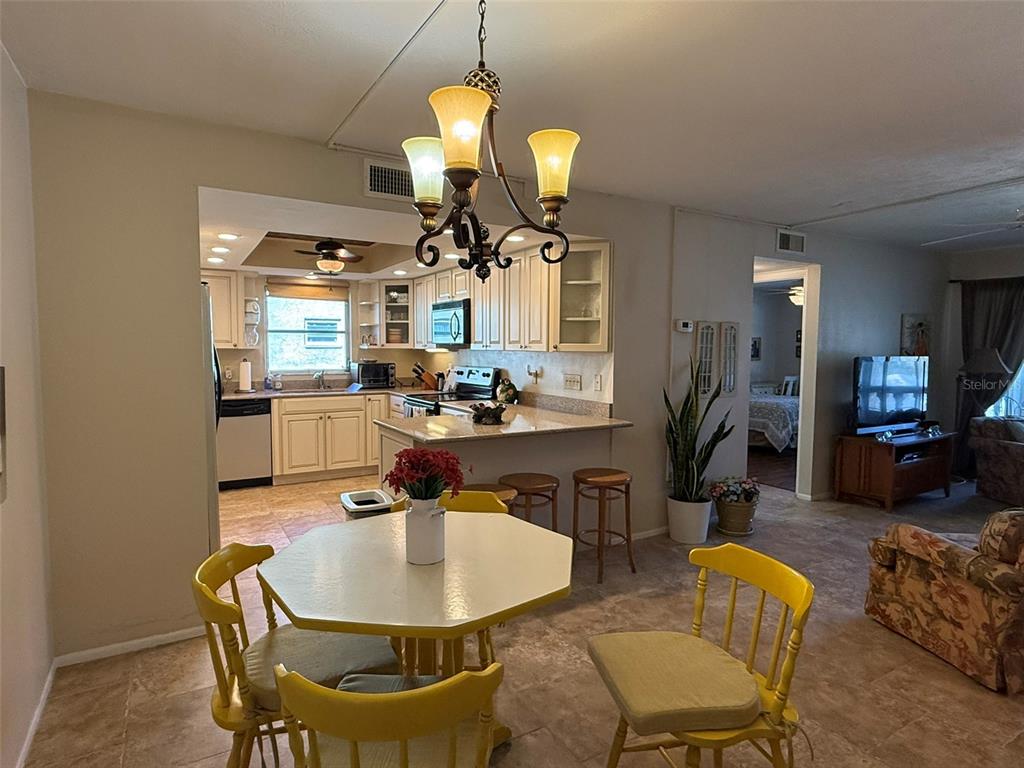 An open-concept dining area with a yellow table and chairs leads into a kitchen — 1250 S PINELLAS AVENUE UNIT 802, TARPON SPRINGS, FL