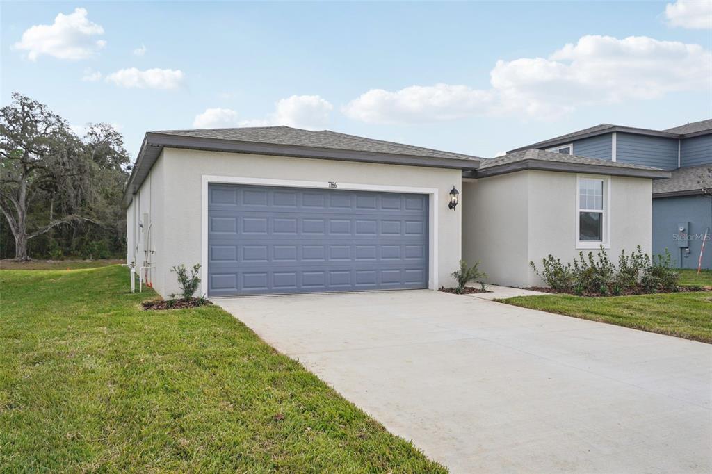 A single-story house with a gray garage door, light stucco exterior, and a concrete driveway — 7186 RAY CREEK DRIVE, BROOKSVILLE, FL