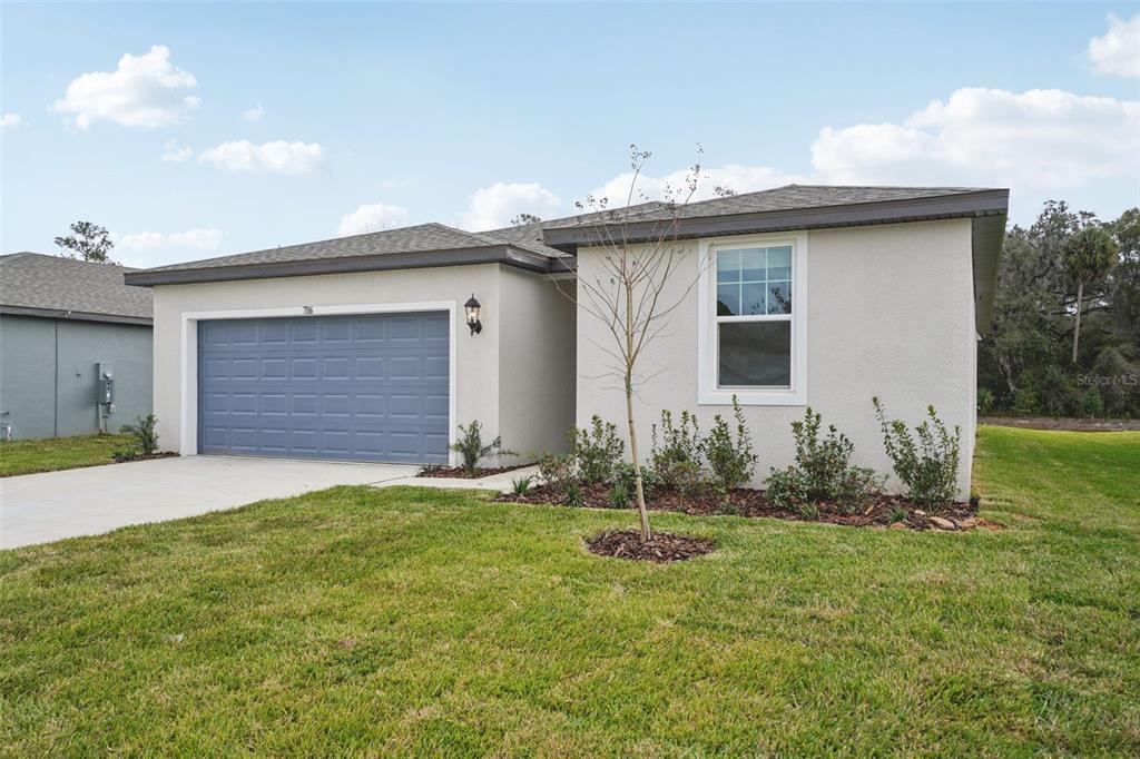 A single-story house with a blue garage door, beige stucco walls, and a grassy lawn — 7186 RAY CREEK DRIVE, BROOKSVILLE, FL