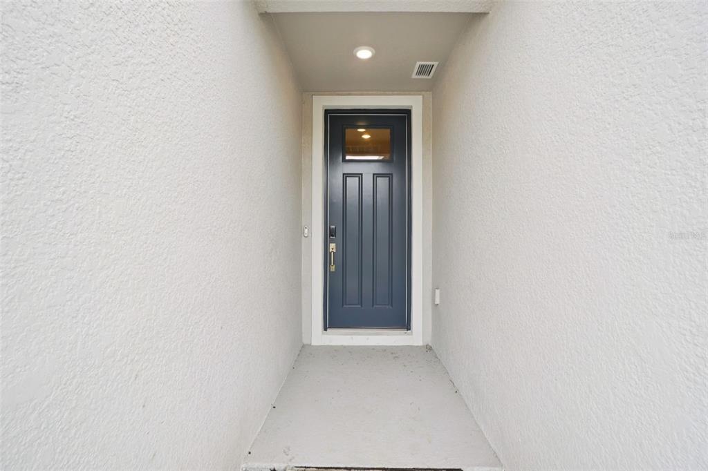 A dark blue front door is centered in a recessed, light-colored stucco entryway — 7186 RAY CREEK DRIVE, BROOKSVILLE, FL
