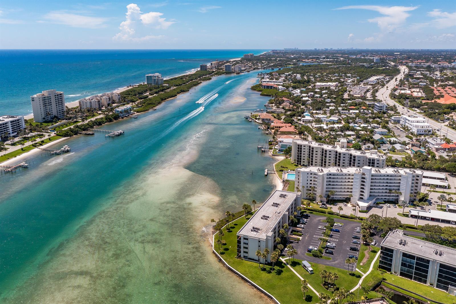 An aerial view shows a coastal waterway with apartment buildings, boats, and a sandy beach — 100 Intracoastal Place # 205, Jupiter FL 33469, JUPITER, FL