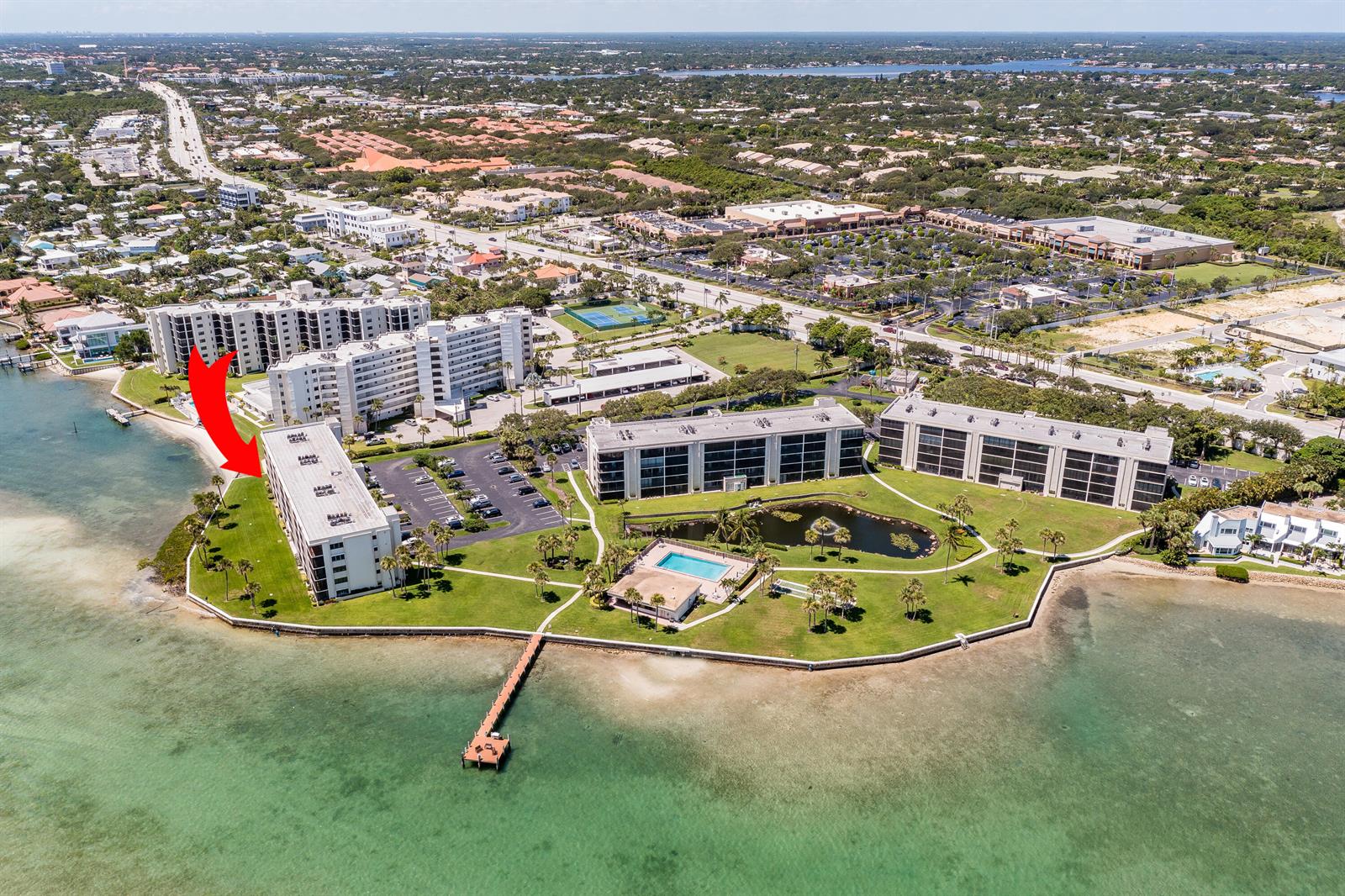 An aerial view shows waterfront apartment buildings with a pool, pond, and wooden pier — 100 Intracoastal Place # 205, Jupiter FL 33469, JUPITER, FL