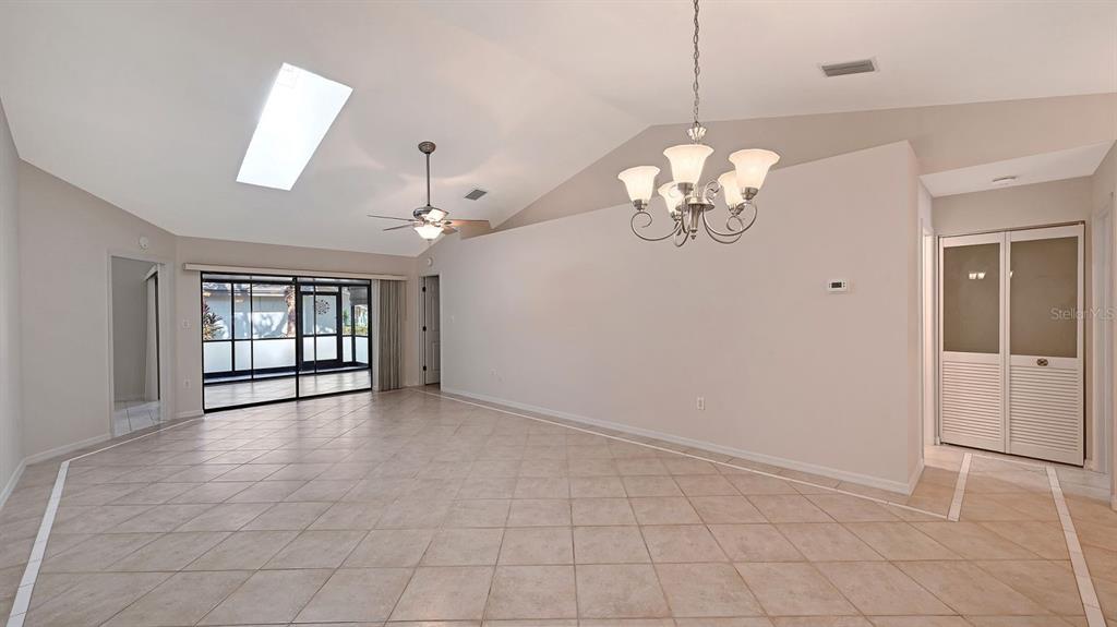 A bright, empty living room features vaulted ceilings, a chandelier, tile flooring, and sliding doors — 4799 OAK FOREST DRIVE W UNIT 43, SARASOTA, FL