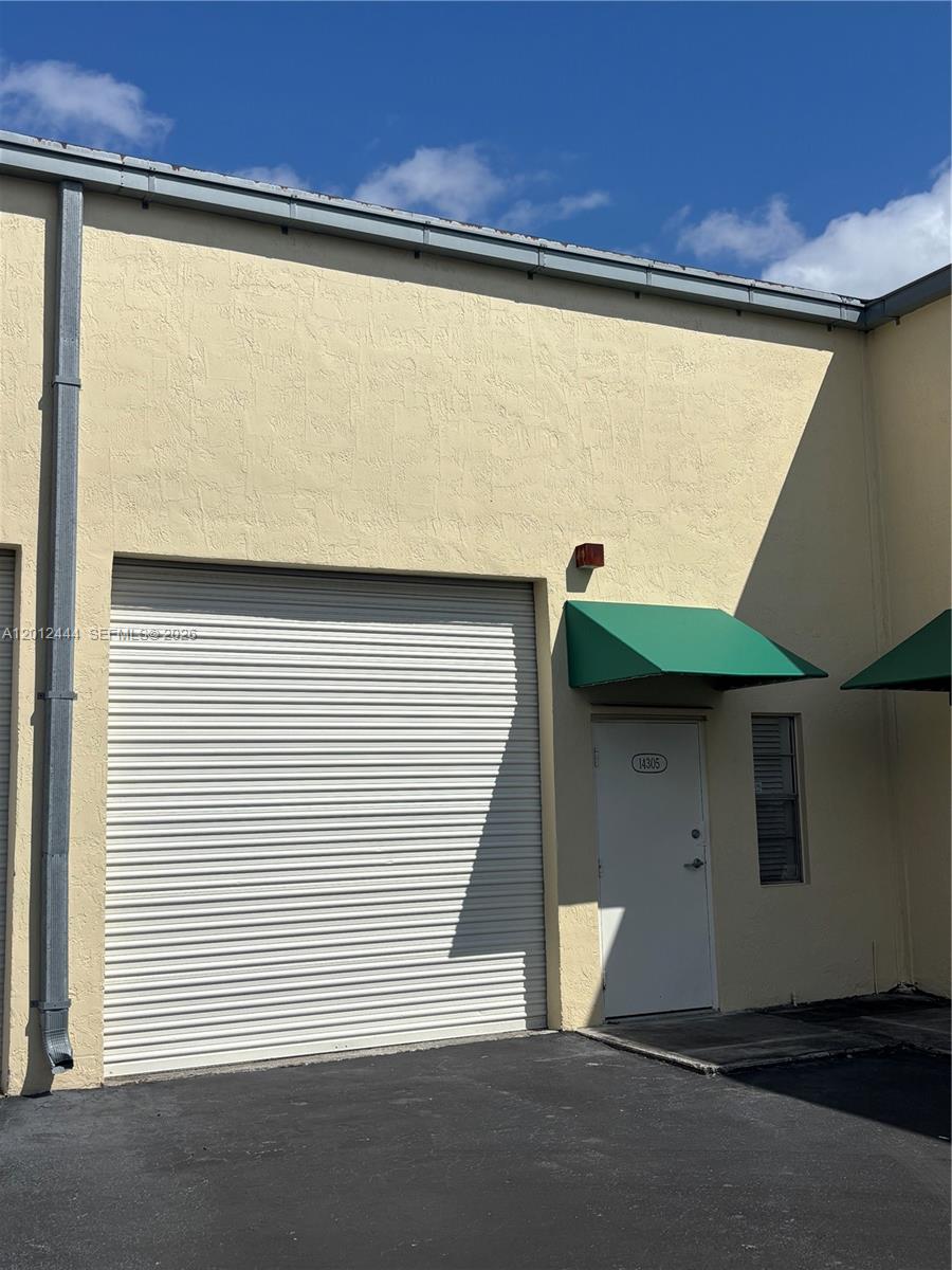 This exterior view shows a commercial building with a roll-up door and a pedestrian entrance — 14305 SW 142nd St, Miami FL 33186, MIAMI, FL