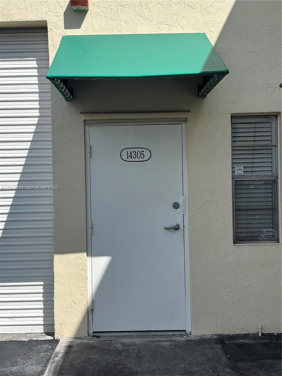 A white door with the number 14305 sits beneath a green awning next to a window — 14305 SW 142nd St, Miami FL 33186, MIAMI, FL