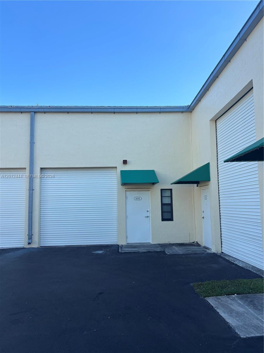 The exterior of a commercial building features two roll-up doors and two pedestrian entry doors — 14305 SW 142nd St, Miami FL 33186, MIAMI, FL