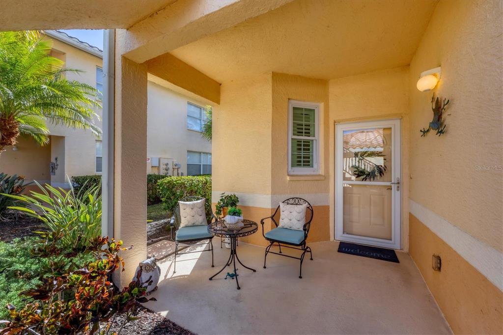A covered patio features two chairs, a small table, and a glass-paneled front door — 4213 VICENZA DRIVE UNIT A2, VENICE, FL