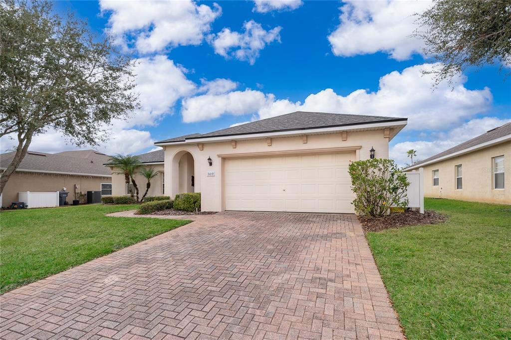 A single-story house with a beige stucco exterior, a two-car garage, and a brick driveway — 569 BURFORD CIRCLE, DAVENPORT, FL