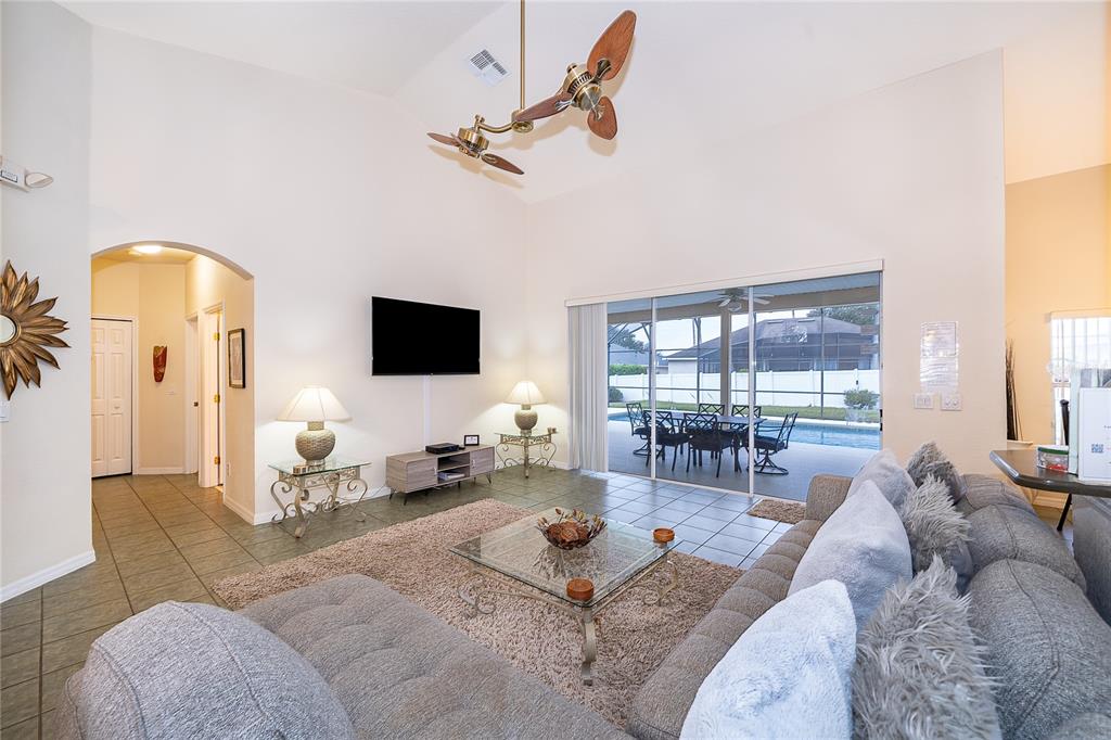 A living room with a vaulted ceiling, tiled floors, and a sliding door to a pool — 569 BURFORD CIRCLE, DAVENPORT, FL