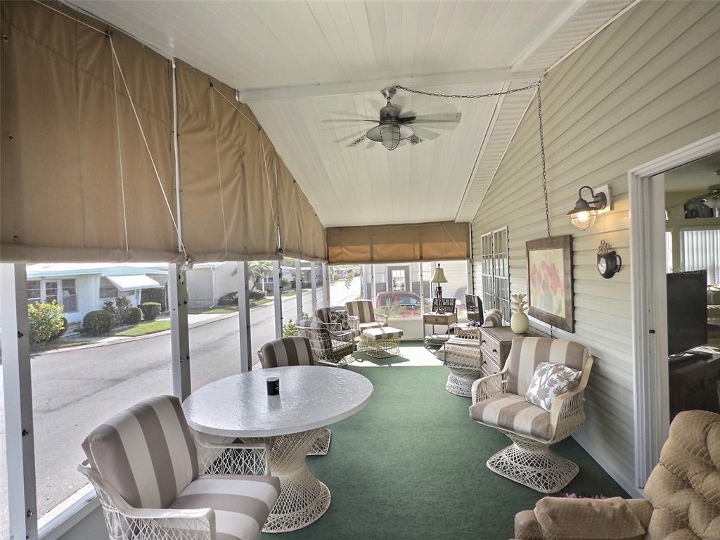 A screened-in porch features a green carpet, white wicker furniture, and tan roll-down shades — 136 PINDO PALM STREET W, LARGO, FL