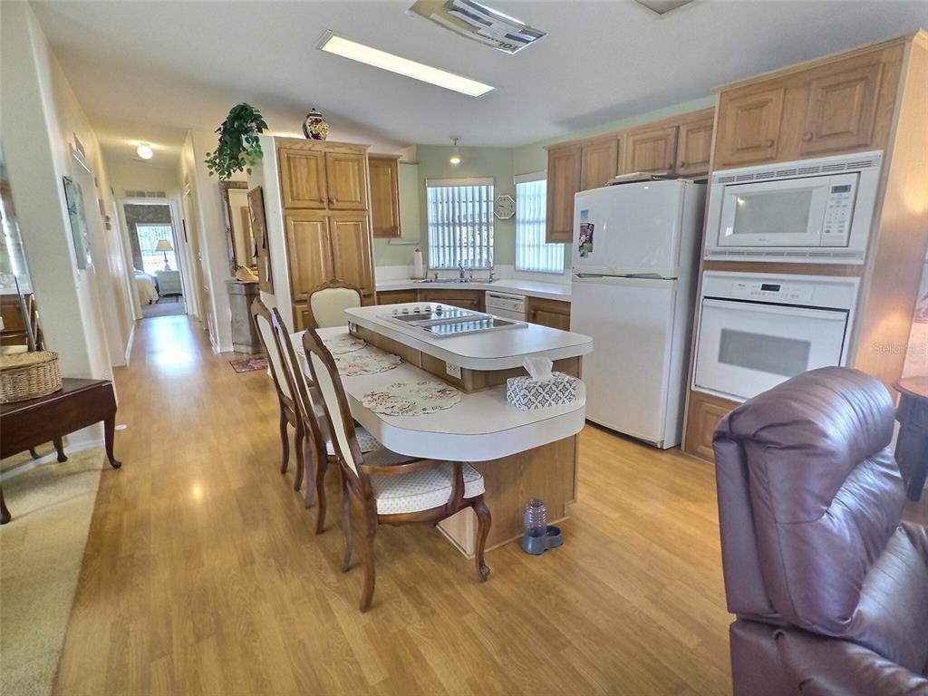 A kitchen features light wood cabinets, white appliances, and a central island with seating — 136 PINDO PALM STREET W, LARGO, FL