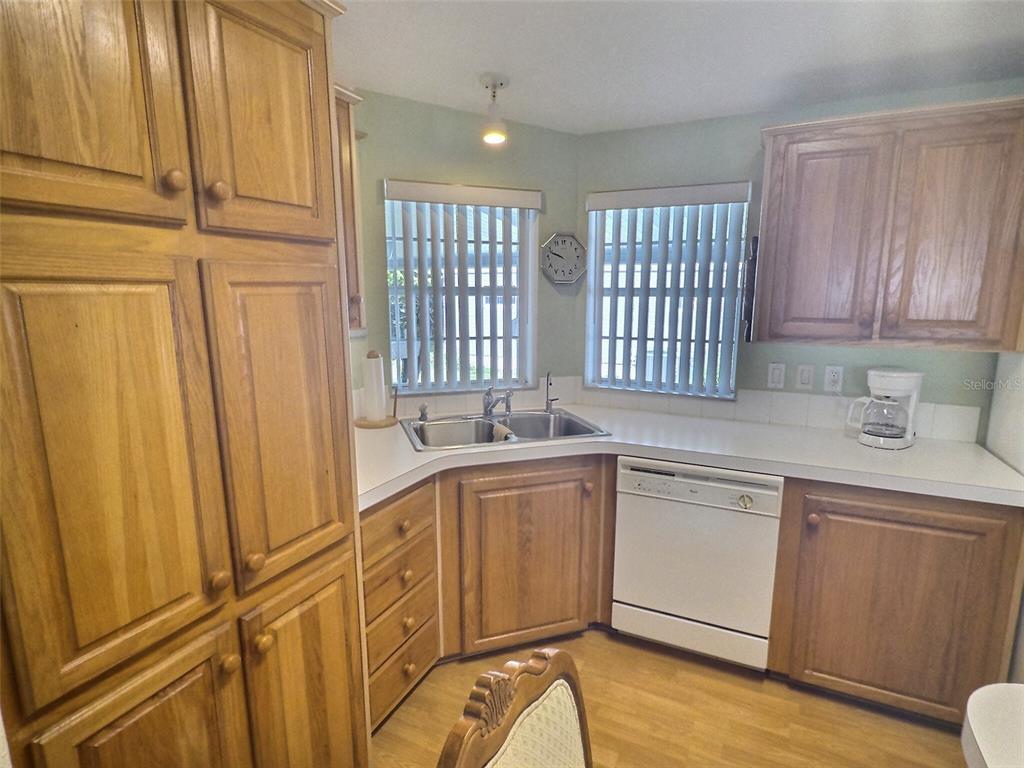 A kitchen features oak cabinets, white countertops, a corner sink, and a white dishwasher — 136 PINDO PALM STREET W, LARGO, FL