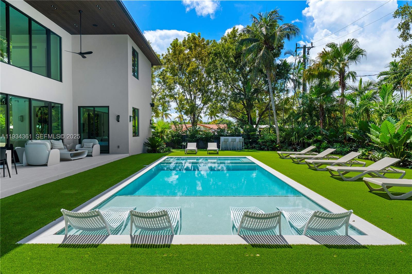 A modern house exterior features a rectangular swimming pool with in-water lounge chairs and artificial turf — 19900 NE 21st Ct, Miami FL 33179, MIAMI, FL