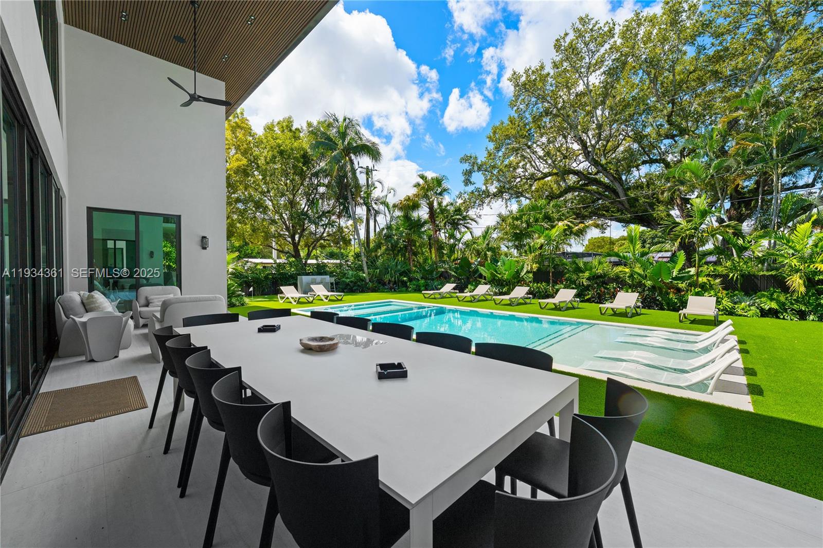 A modern patio features a long dining table overlooking a swimming pool and lawn — 19900 NE 21st Ct, Miami FL 33179, MIAMI, FL
