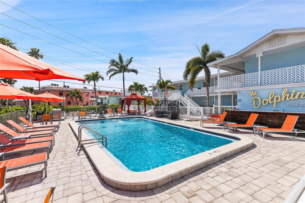 An outdoor swimming pool surrounded by lounge chairs, umbrellas, and a multi-story building — 6801 SUNSET WAY, ST PETE BEACH, FL