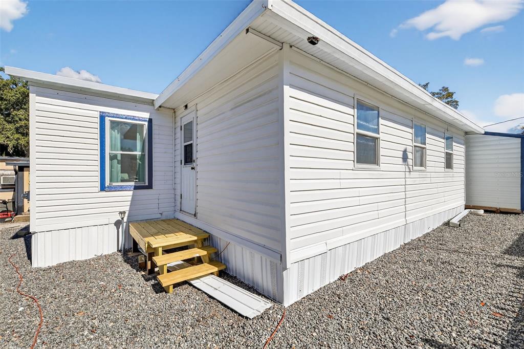 The exterior of a white mobile home features a wooden staircase leading to a side door — 38237 ORIOLE WAY, LEESBURG, FL
